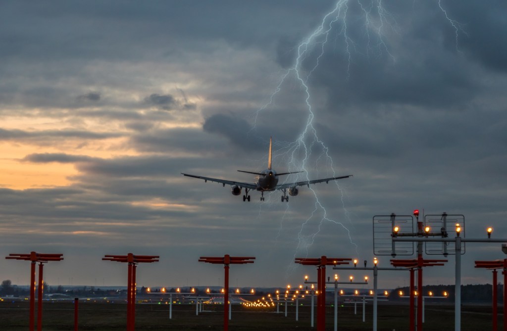 Ein Flugzeug landet bei Gewitter und ein Blitz schlägt am Horizont ein.