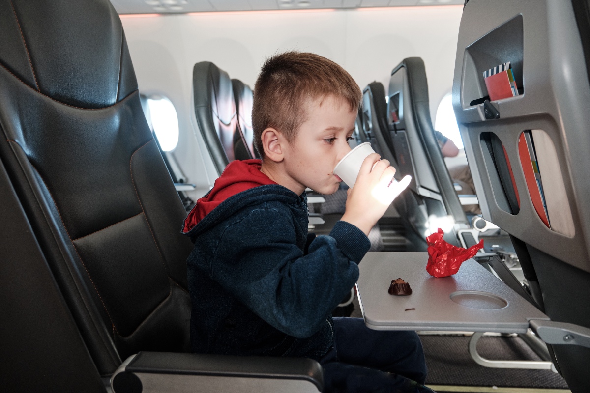 Ein blonder Junge trinkt in einem Flugzeug aus einem Becher.