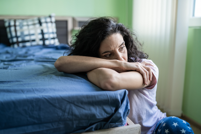 Eine traurige und müde Frau lehnt mit den Armen auf einem Bett im Schlafzimmer