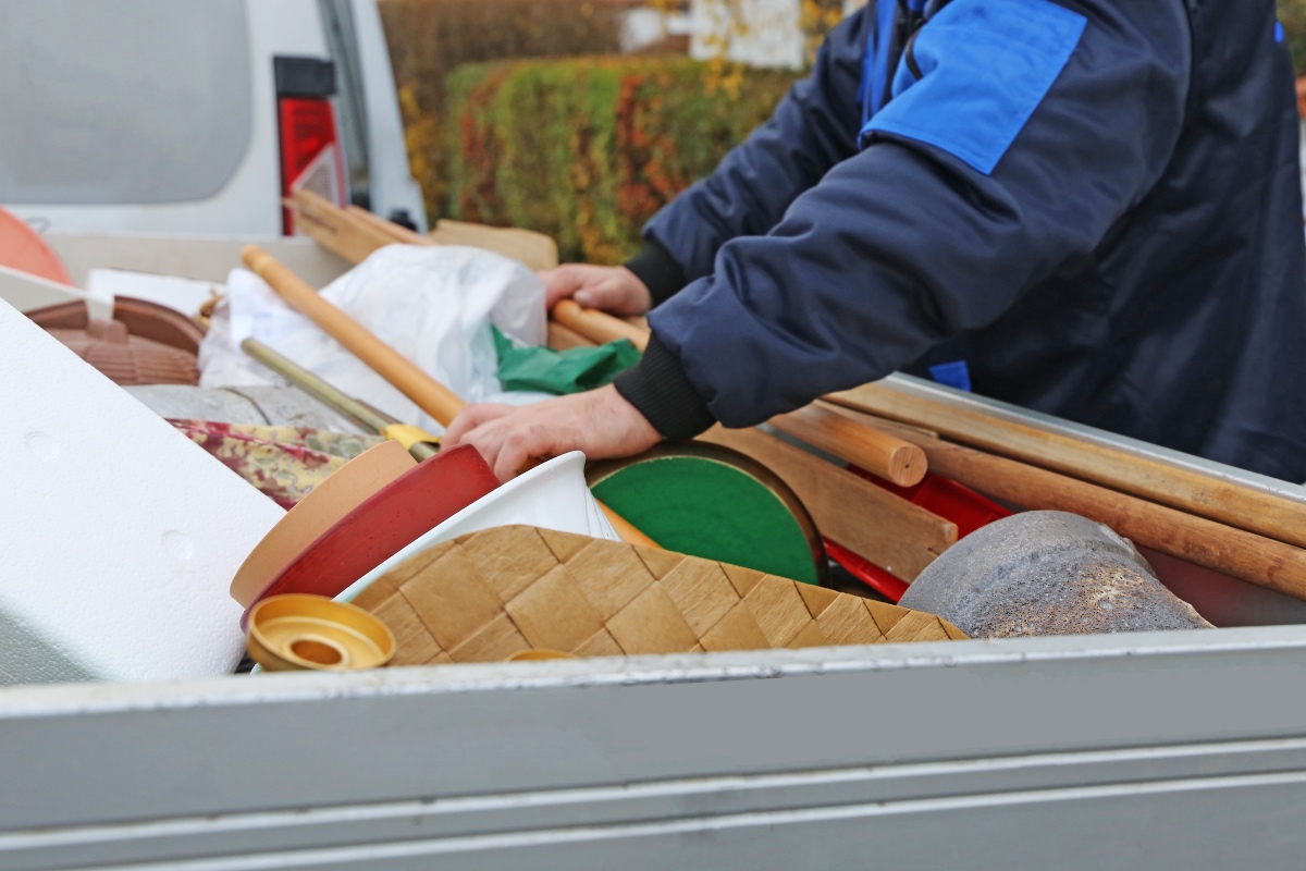 Eine Person in blauem Anzug durchsucht einen Container, der mit Sperrmüll gefüllt ist.