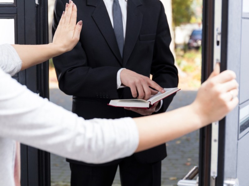 Ein Zeuge Jehovas liest an der Türschwelle einer Frau aus einer Bibel vor.