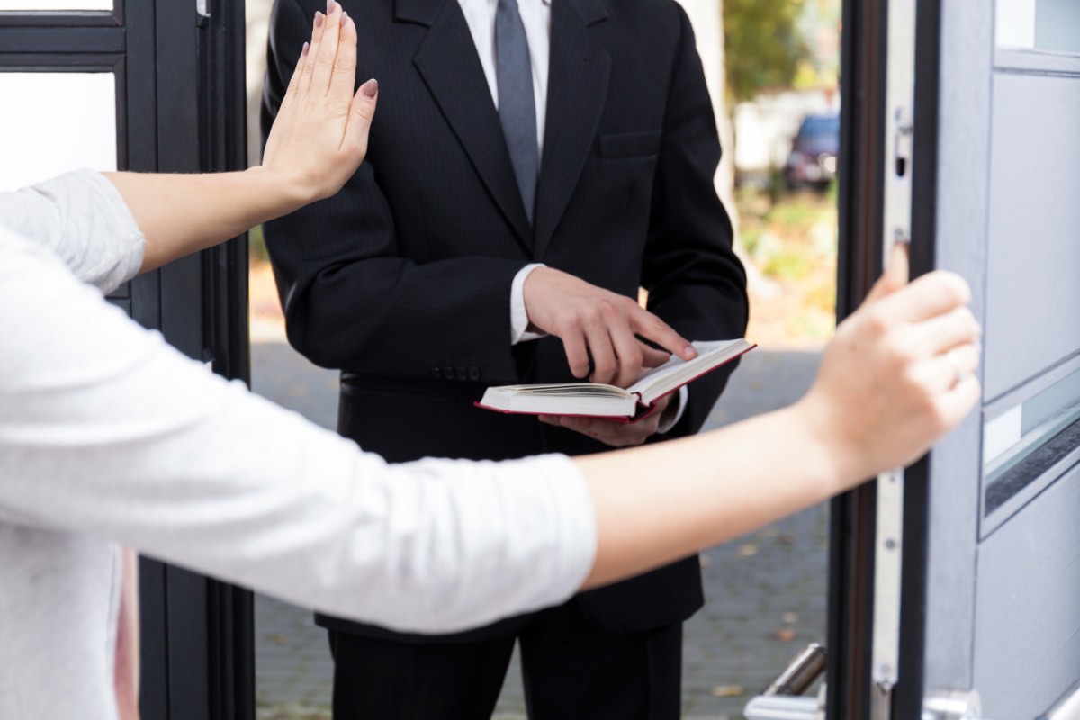 Ein Zeuge Jehovas liest an der Türschwelle einer Frau aus einer Bibel vor.