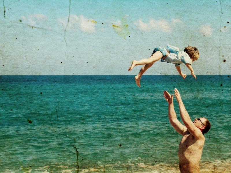 Ein altes Foto von einem Vater, der mit seinem Kind am Strand spielt.