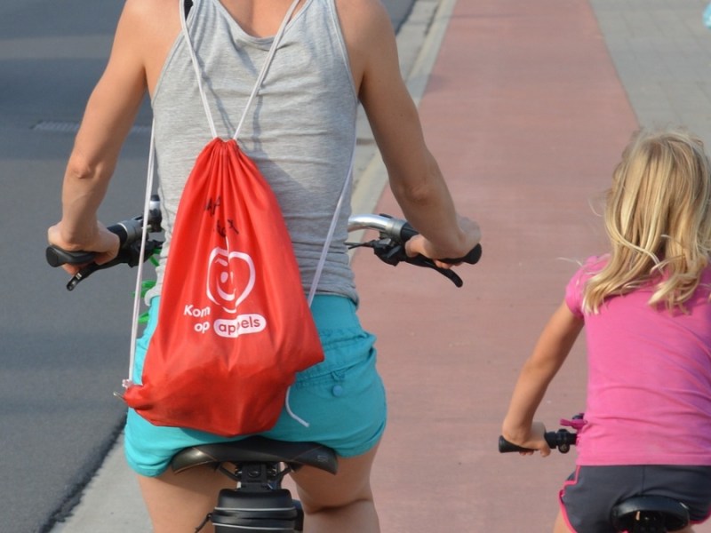 Eine Mutter fährt mit ihrer kleinen Tochter Fahrrad auf einem roten Radweg.