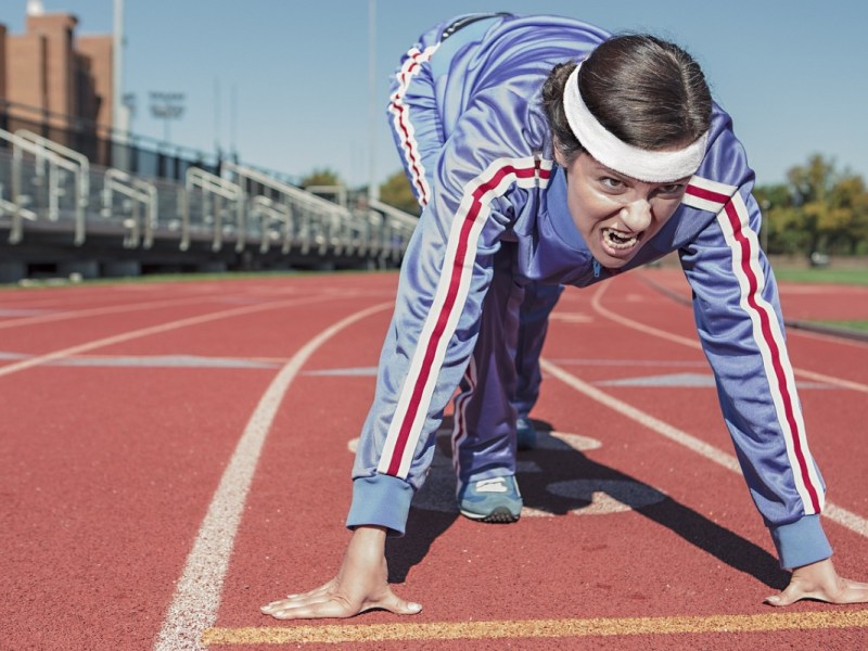 Eine Frau in Sportkleidung geht bei einem Wettlauf im Stadion in Startposition.