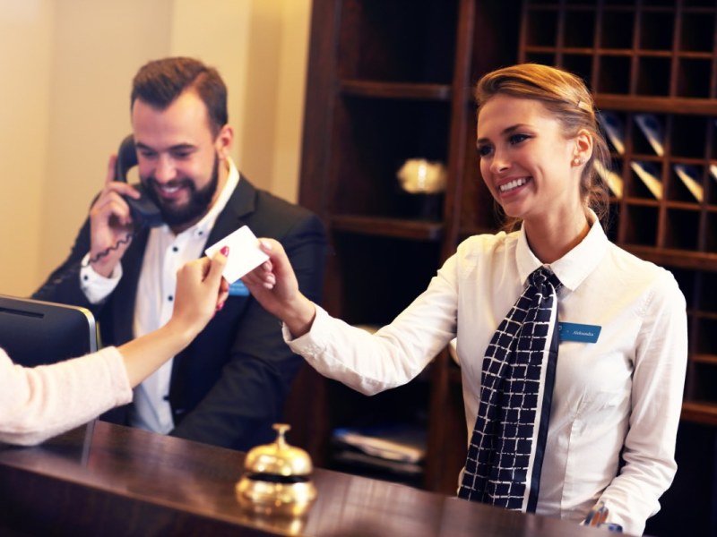 Zwei Angestellte am Empfang eines Hotels geben einem Gast die Zimmerkarte.