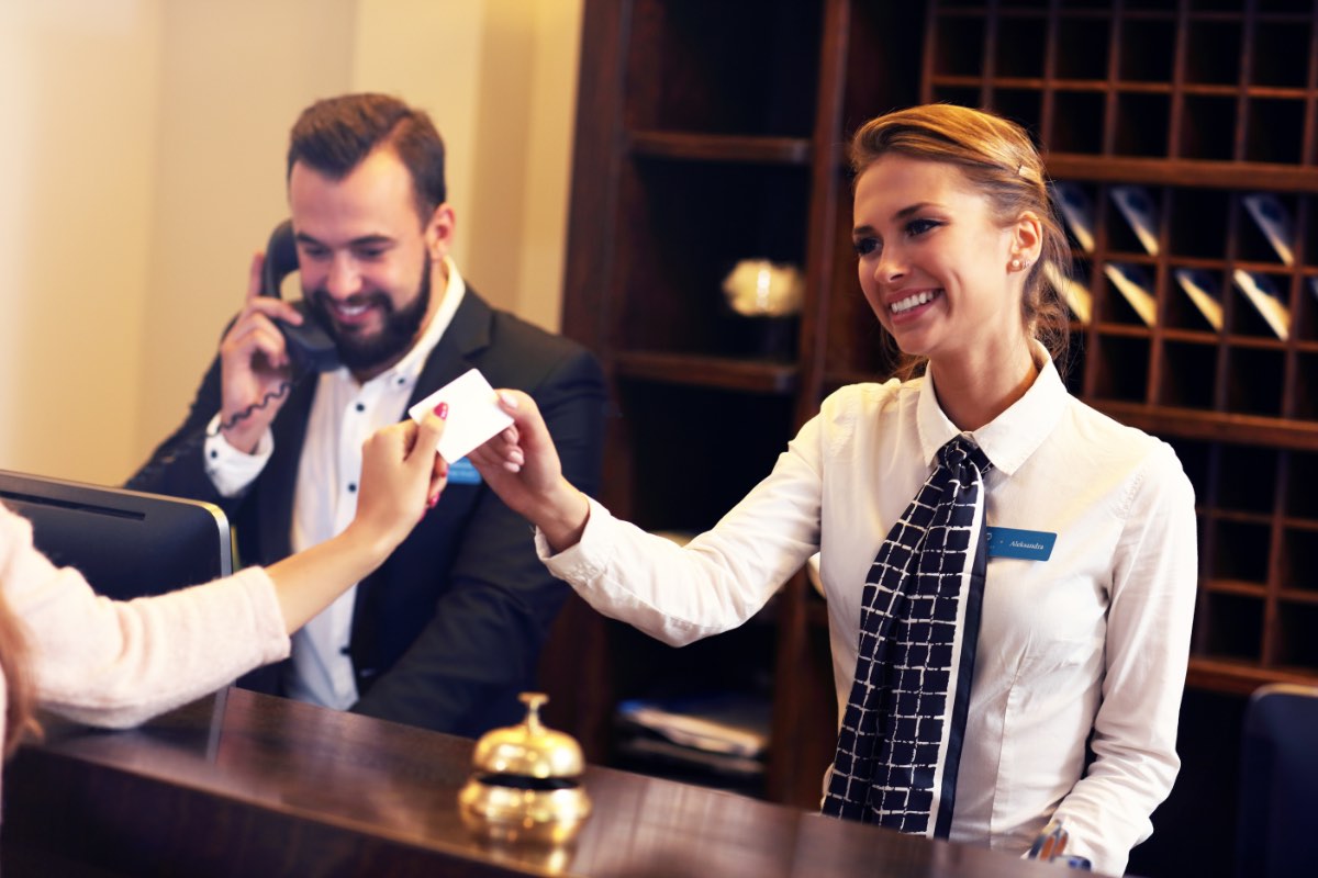 Zwei Angestellte am Empfang eines Hotels geben einem Gast die Zimmerkarte.