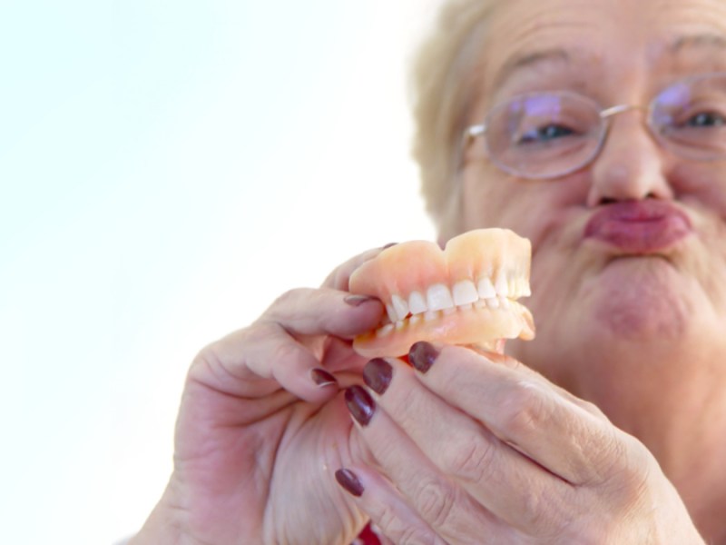 Eine Rentnerin hält ihr Gebiss in der Hand und schürzt die Lippen.