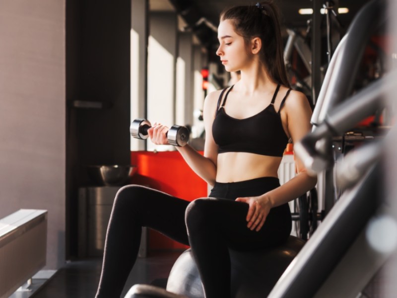 Junge Frau trainiert mit einer Hantel im Fitnessstudio.