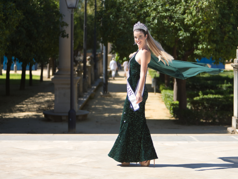 Eine Schönheitskönigin in einem grünen Kleid vor einer Allee fotografiert.