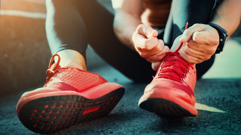 Ein Mann, der an einem sonnigen Tag im Freien läuft, bindet seine Joggingschuhe.